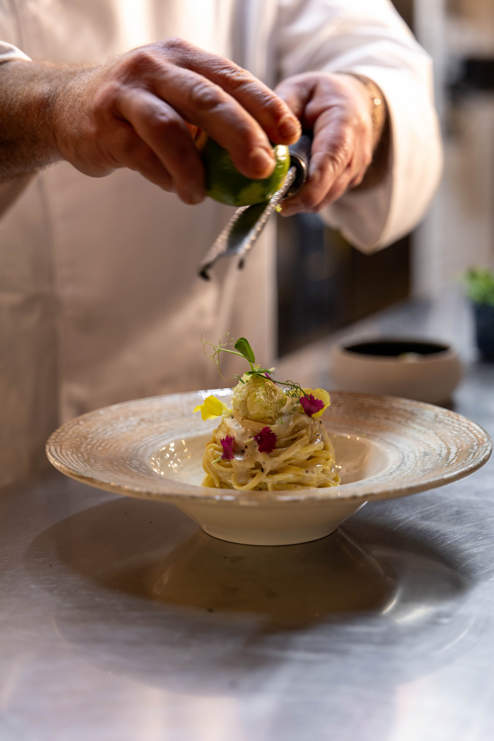 Le chef Pasquale Lanziotti râpe du citron vert sur une assiette de tagliatelles signature au Boscolo Hôtel & Spa Nice