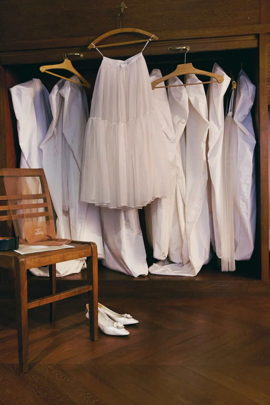 Toiles de haute couture Dior suspendues dans une armoire d'atelier, chaise en bois et escarpins blancs
