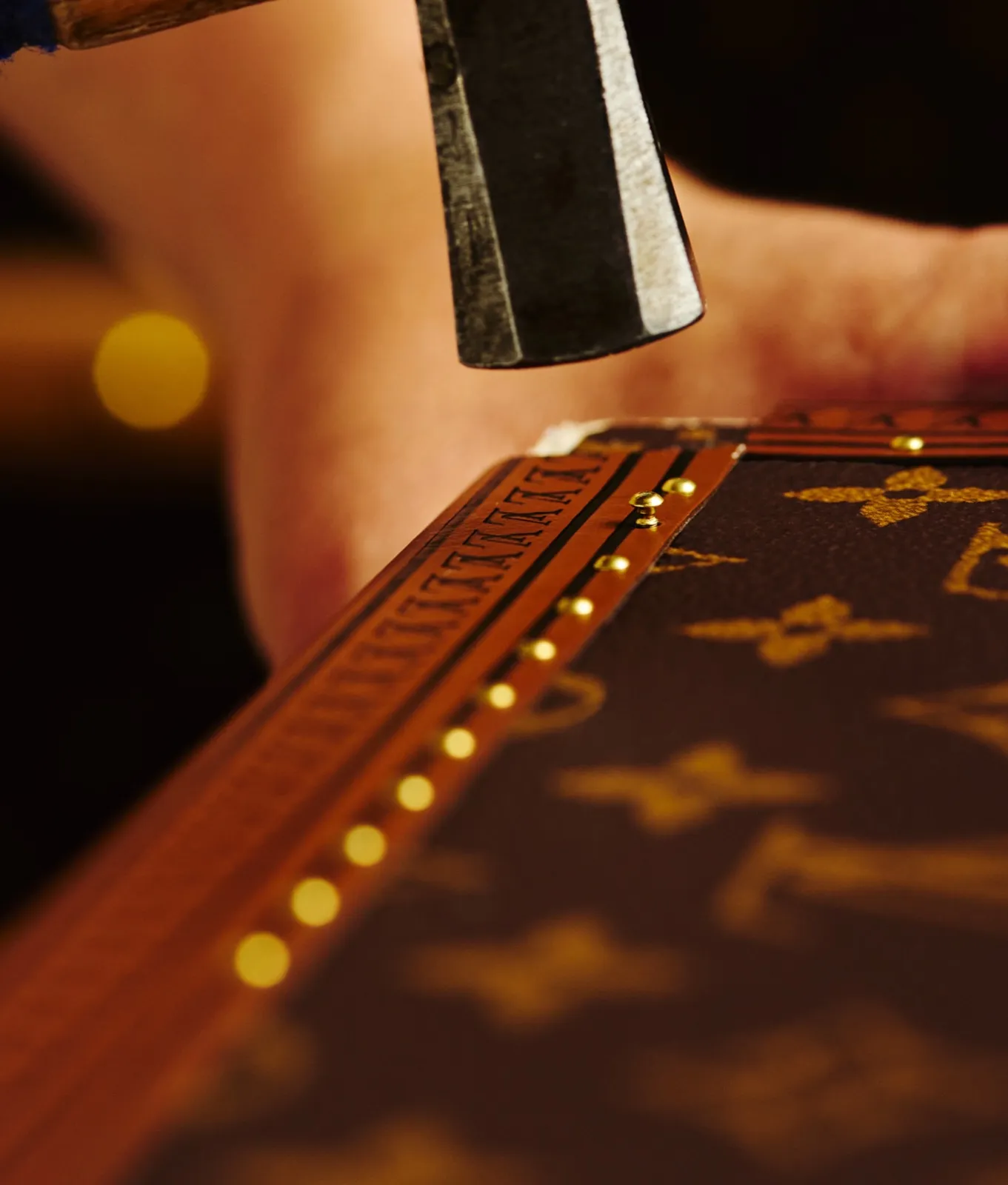 Artisan Louis Vuitton clouant la bordure d'une malle en toile Monogram, gros plan sur le marteau