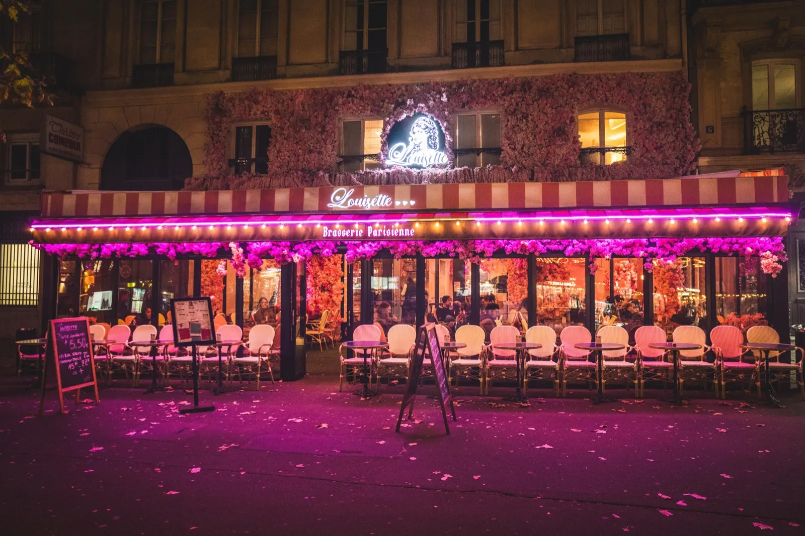 Façade nocturne de la brasserie Louisette sur le boulevard Saint-Denis, terrasse fleurie éclairée de rose