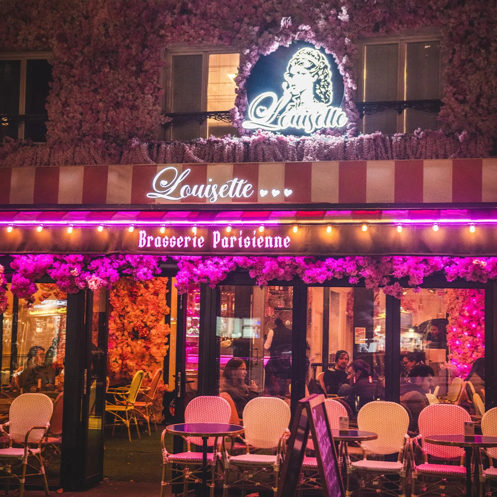 Enseigne néon et marquise rayée de la brasserie parisienne Louisette, terrasse aux chaises roses