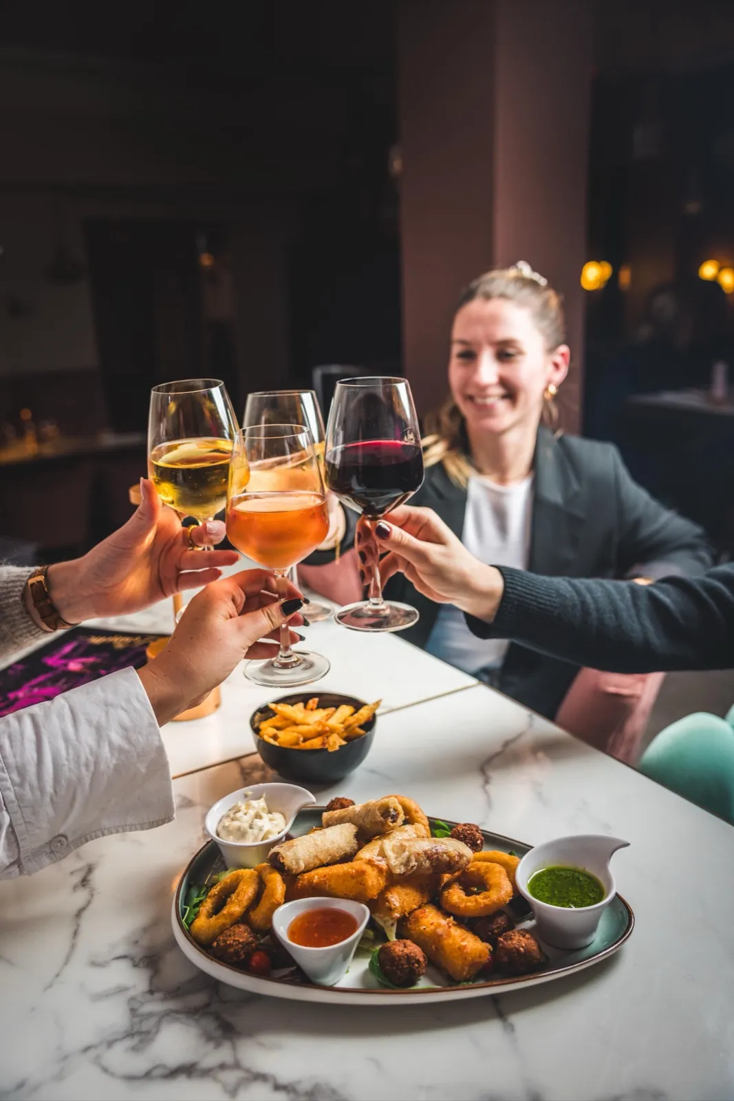 Convives trinquant autour d'une table en marbre garnie de planches à partager chez Louisette