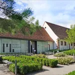 Bâtiment vitré du musée Lalique à Wingen-sur-Moder, dans son jardin de buis taillés, sous un ciel bleu