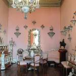 Salon aux murs rose poudré orné de porcelaines, d'un grand lustre à pampilles et de mobilier ancien