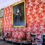 Salon aux murs tendus de damas rouge à motifs floraux, portrait en pied et canapé assorti au palais de Nieborów