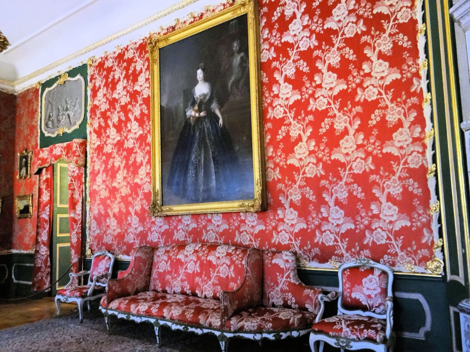 Salon aux murs tendus de damas rouge à motifs floraux, portrait en pied et canapé assorti au palais de Nieborów