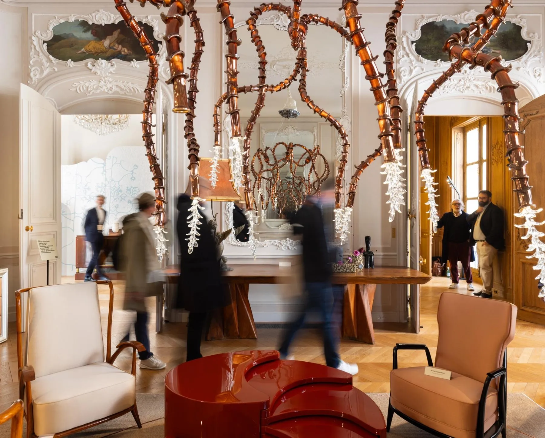 Salon aux décors de stuc de l'hôtel de Maisons avec suspension en verre ambré, fauteuils et table basse laquée rouge pendant Design Miami Paris 2026