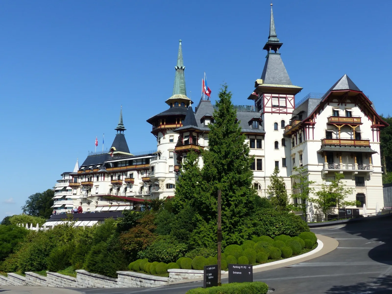 Façade néo-Renaissance et tourelles de l'hôtel The Dolder Grand dominant Zurich, sous un ciel bleu et entre les arbres