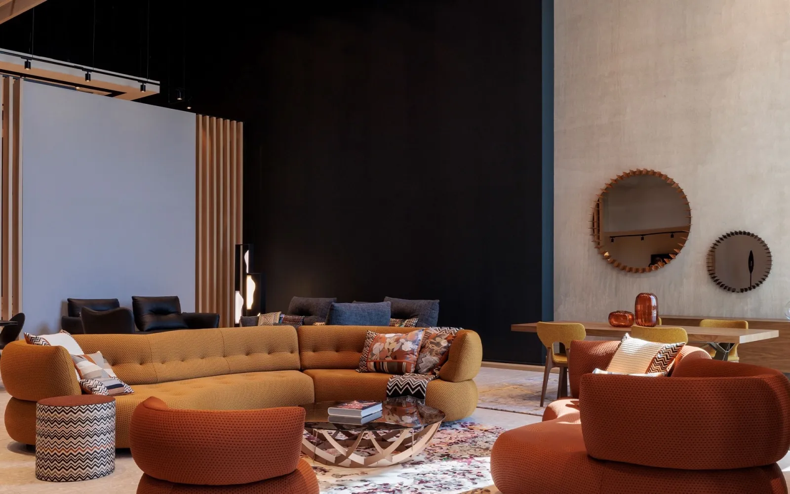 Salon aux canapés arrondis ocre et fauteuils terracotta, miroirs en soleil et mur sombre dans un showroom de design