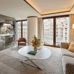Salon d'une suite du Bvlgari Hotel Paris : canapé clair, table basse ovale et bijou exposé au mur, vue sur les toits