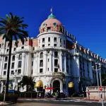 Façade blanche et dôme rose de l'hôtel Negresco sur la Promenade des Anglais à Nice, entre les palmiers