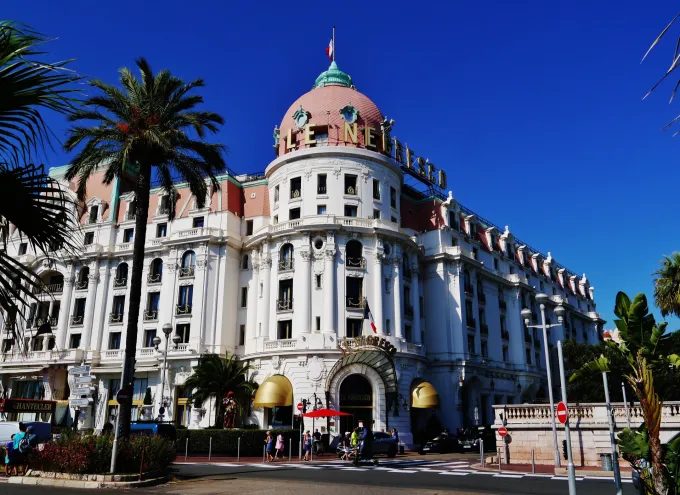 Façade blanche et dôme rose de l'hôtel Negresco sur la Promenade des Anglais à Nice, entre les palmiers