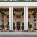 Entrée colonnée de l'hôtel Six Senses London au Whiteley, façade en pierre claire ornée de plantes retombantes