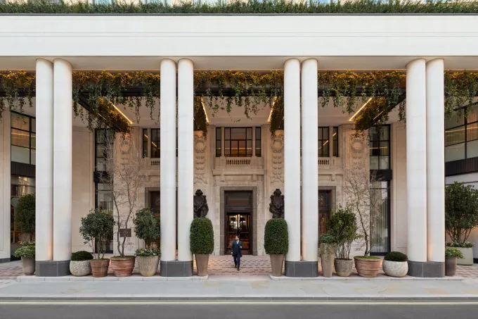 Entrée colonnée de l'hôtel Six Senses London au Whiteley, façade en pierre claire ornée de plantes retombantes
