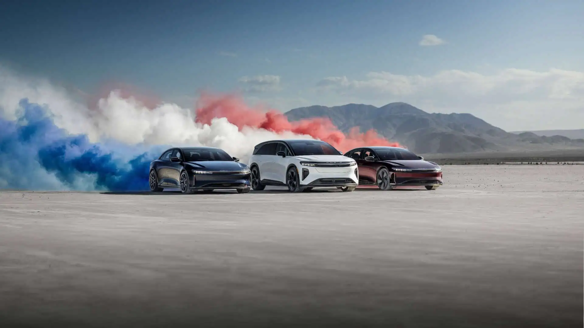 Deux Lucid Air et un Lucid Gravity devant des fumigènes bleu blanc rouge dans le désert
