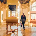 Omar Sy en Assane Diop traverse un salon doré où des couronnes reposent dans des vitrines, photo officielle de Lupin partie 4