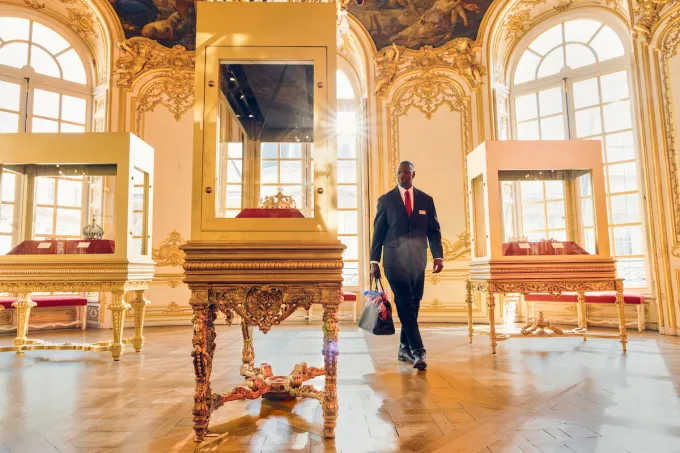 Omar Sy en Assane Diop traverse un salon doré où des couronnes reposent dans des vitrines, photo officielle de Lupin partie 4