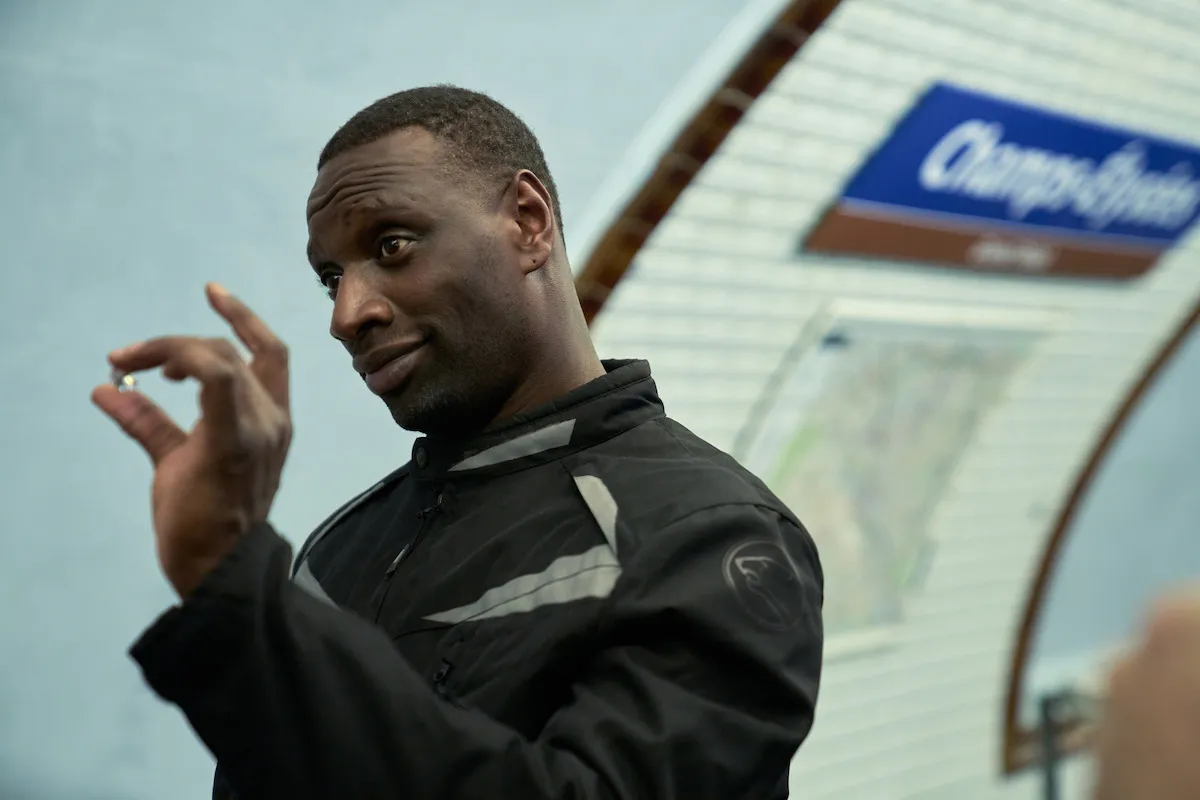 Omar Sy tient une petite pierre entre ses doigts sur un quai de métro à l'enseigne Champs-Élysées, Lupin partie 4