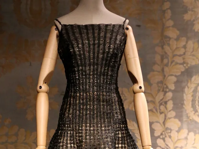 Robe haute couture noire ajourée de Dior présentée sur un mannequin de bois devant une tenture à motifs dorés