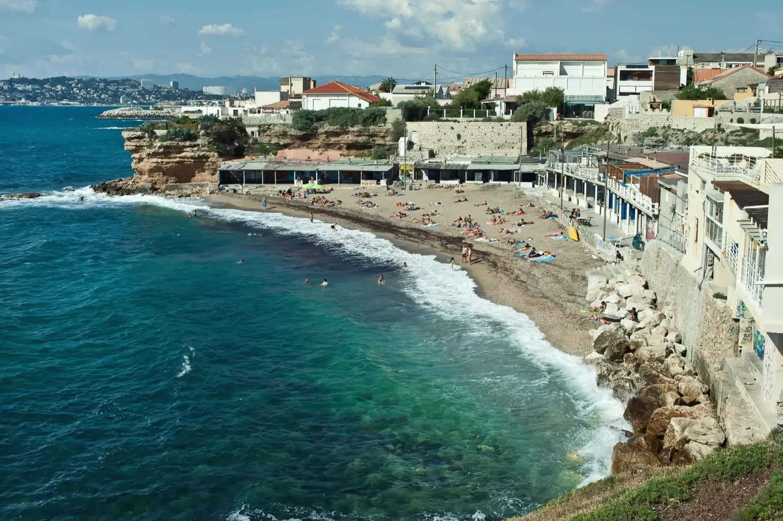Vue sur la plage de Bonne Brise à Marseille, mer turquoise, rivage rocheux et immeubles en bord de mer