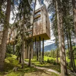 Hôtel My Arbor suspendu sur de hauts pilotis au milieu des sapins de la forêt de la Plose, avec les montagnes au loin