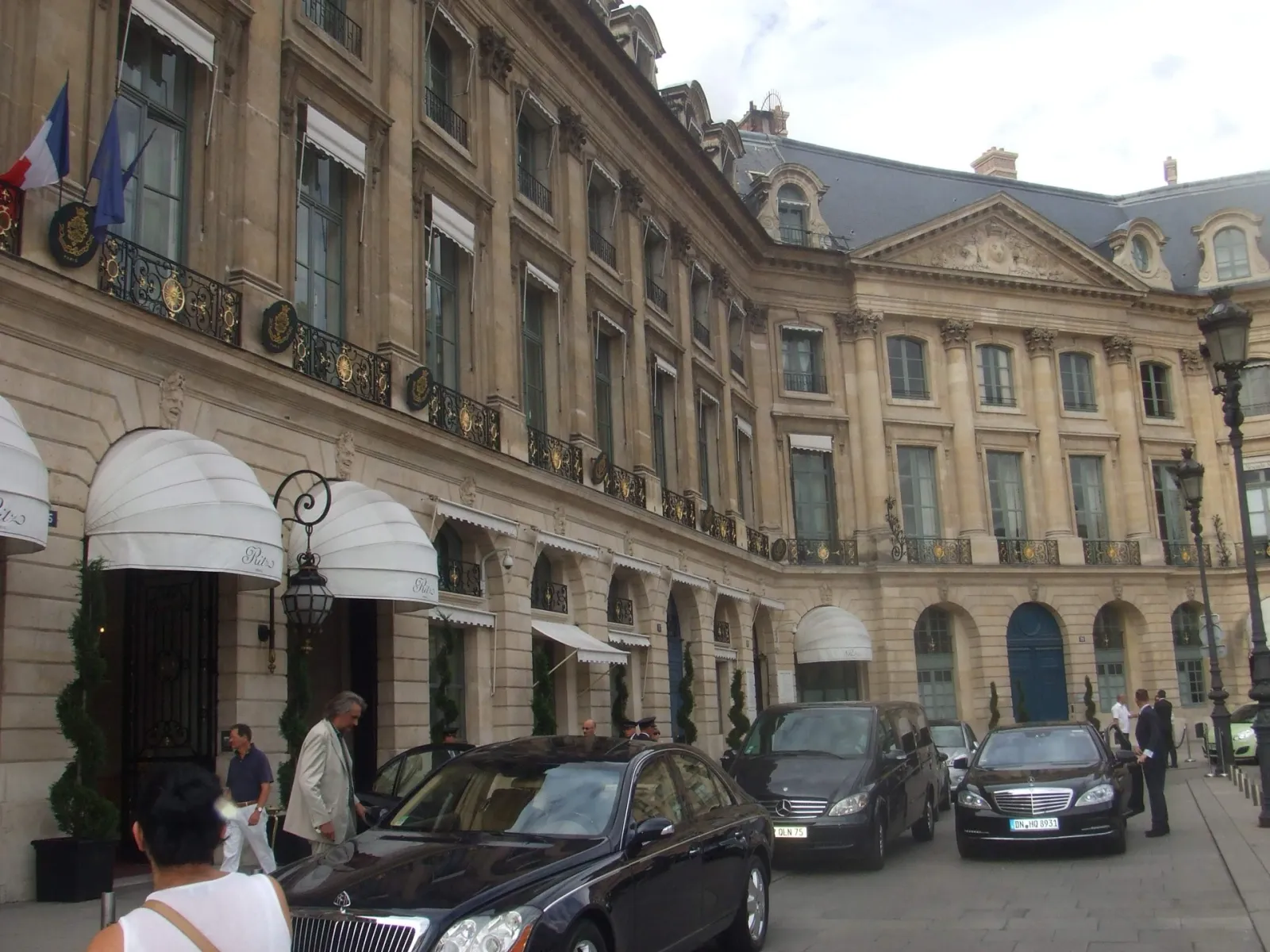 Façade classique du Ritz Paris place Vendôme, auvents blancs au rez-de-chaussée et berlines devant l'entrée
