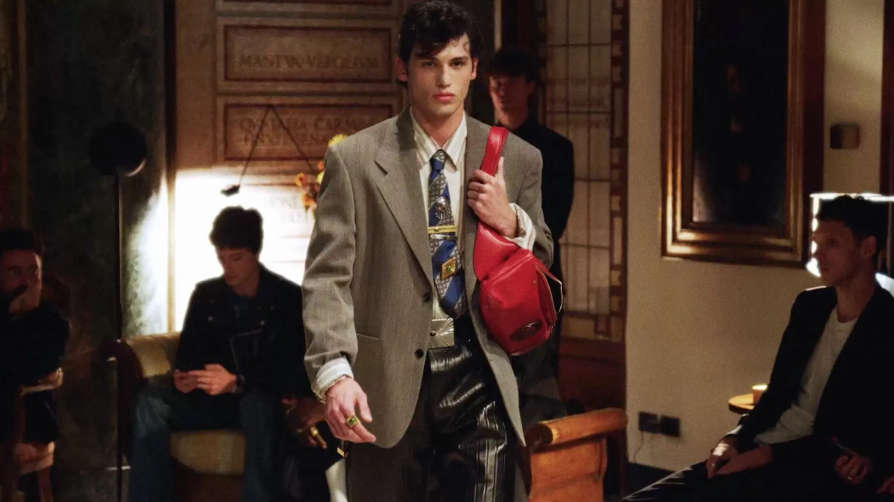 Silhouette masculine Versace en costume beige et sac rouge lors d'une présentation